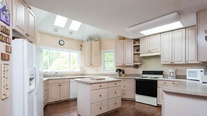 A kitchen with wooden flooring, white cabinets, a stove, a microwave, and a refrigerator.