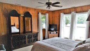 A bedroom with a bed, a television on a stand, a ceiling fan, and a large mirror.