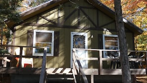 A wooden cabin with a porch, a set of stairs leading up to the entrance, and a small deck area.