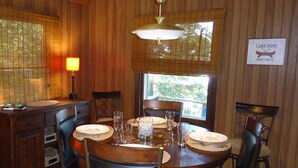 A wooden dining room with a table set for four, a lamp, and a sign reading "Lake Home Sweet Home".