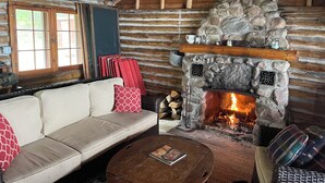 A log cabin interior with a stone fireplace, a sofa, and a coffee table. - Rustic Authentic Michigan Log Cabin (Beaver Island)