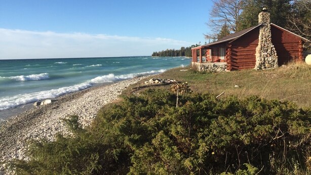 A log cabin by a rocky shoreline with a view of the ocean. - Rustic Authentic Michigan Log Cabin (Beaver Island)