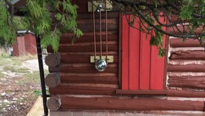 A log cabin with a red exterior, a metal door, and a stone pathway leading to the entrance. - Rustic Authentic Michigan Log Cabin (Beaver Island)