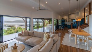A spacious living area with a large sofa, dining table, and chairs, overlooking a scenic view. - Cowries - Hamilton Island (Hamilton Island)