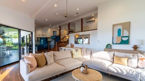 A spacious living area with a large L-shaped sofa, a round wooden coffee table, and a dining area with a table and chairs. - Cowries - Hamilton Island (Hamilton Island)