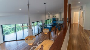 A spacious kitchen with a large island, a dining area with a wooden table and chairs, and a view of the outdoors through large sliding doors. - Cowries - Hamilton Island (Hamilton Island)