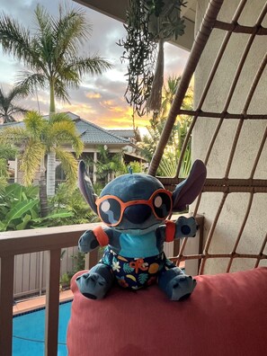 Een pluche speeltje op een balkon, met een zwembad en palmbomen op de achtergrond.