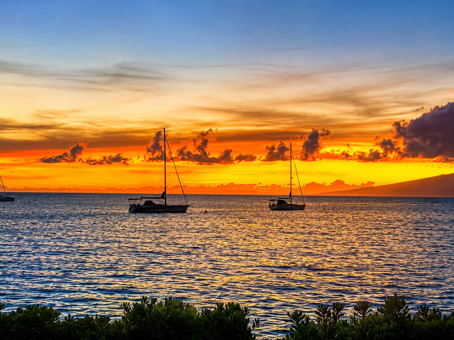 A sunset over a calm sea with two sailboats.