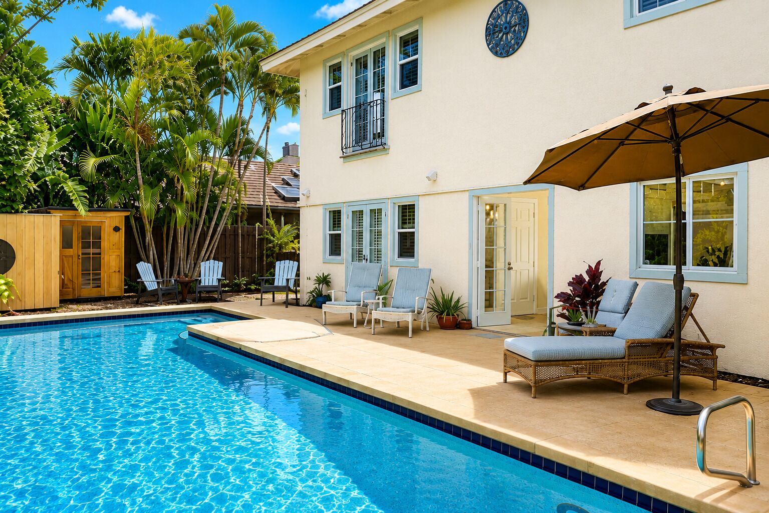 A swimming pool with lounge chairs and a covered umbrella, surrounded by a house with a balcony and a wooden shed.