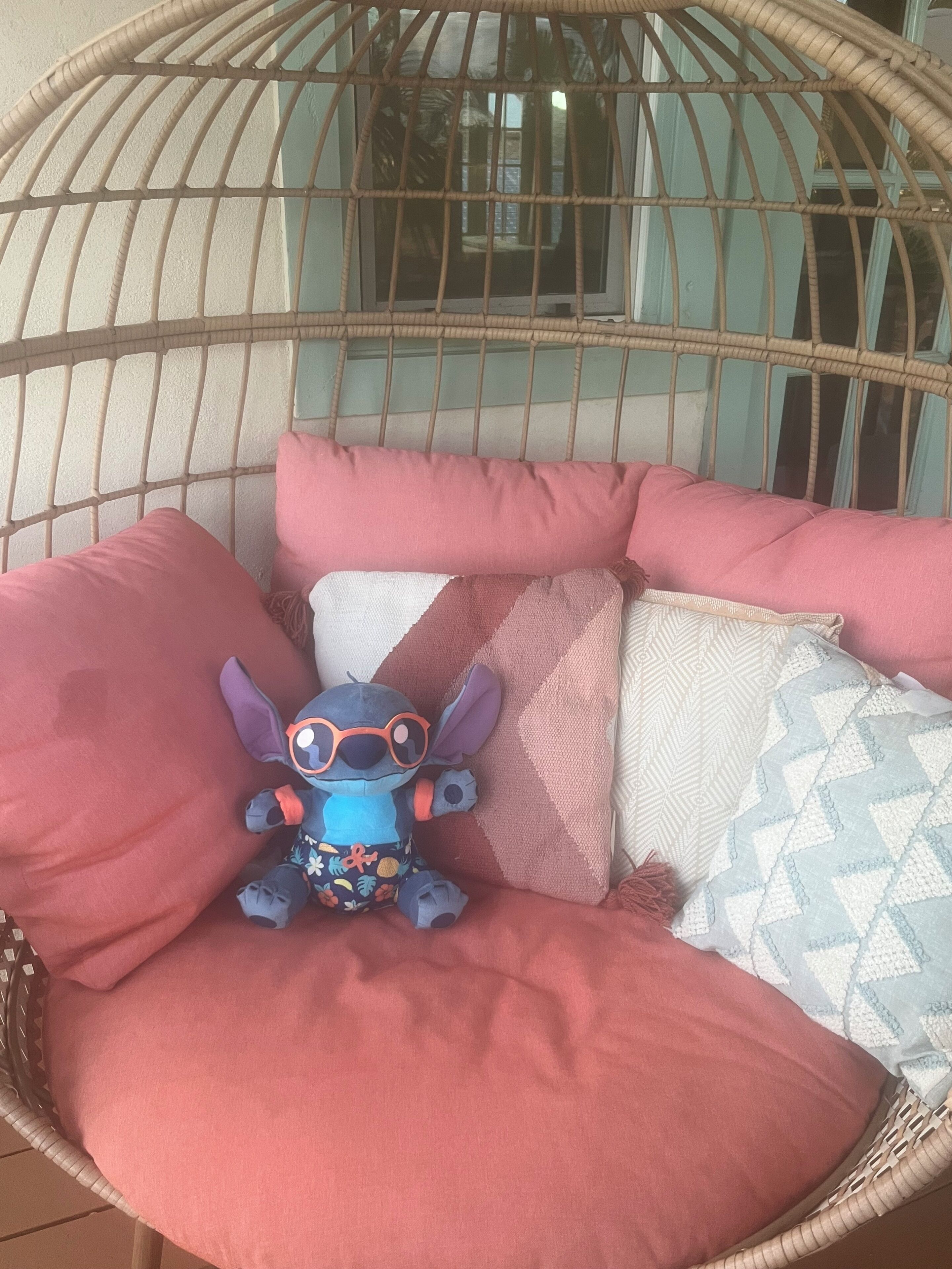 A wicker chair with a plush toy and multiple cushions.