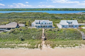 Ein Strandgrundstück mit mehreren Häusern, darunter ein zentrales Haus mit einer großen Veranda, und einem Weg zum Strand.