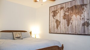 Un dormitorio con cama, un mapa del mundo en la pared, un ventilador de techo y una lámpara.