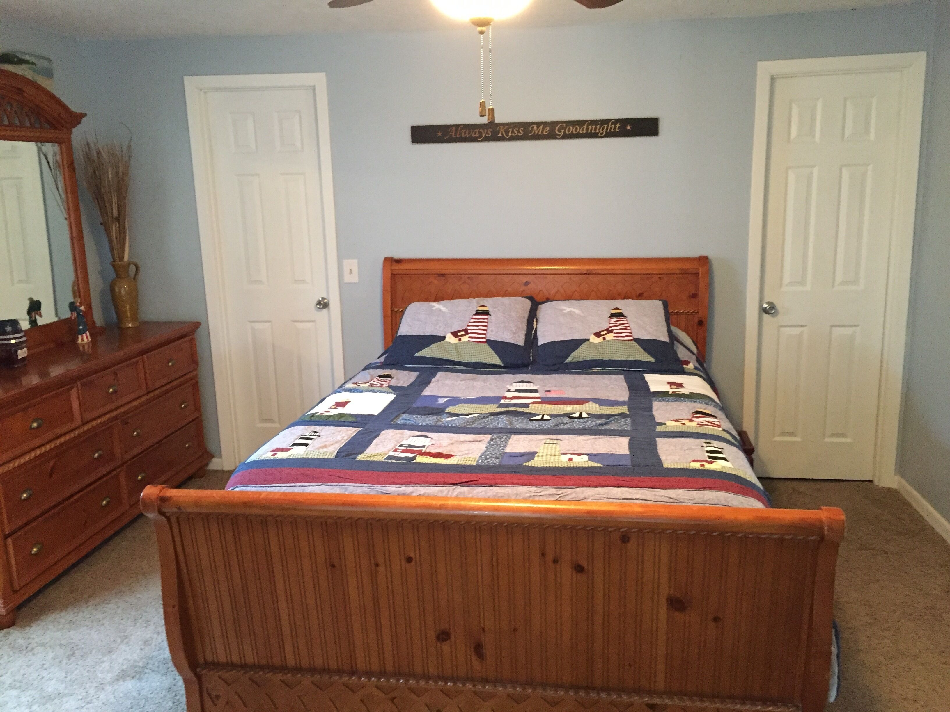 Un dormitorio con una cama de madera, un tocador y un espejo. Hay un letrero en la pared que dice 'Always Kiss Me Goodnight'.