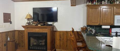 A kitchen with wooden cabinets, a fireplace, a television, and a bar area with bottles.