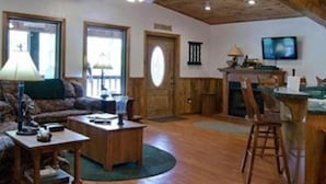 Ein Wohnzimmer mit Holzboden, einem Fernseher, einem Kamin und einem Essbereich mit Tisch und Stühlen.