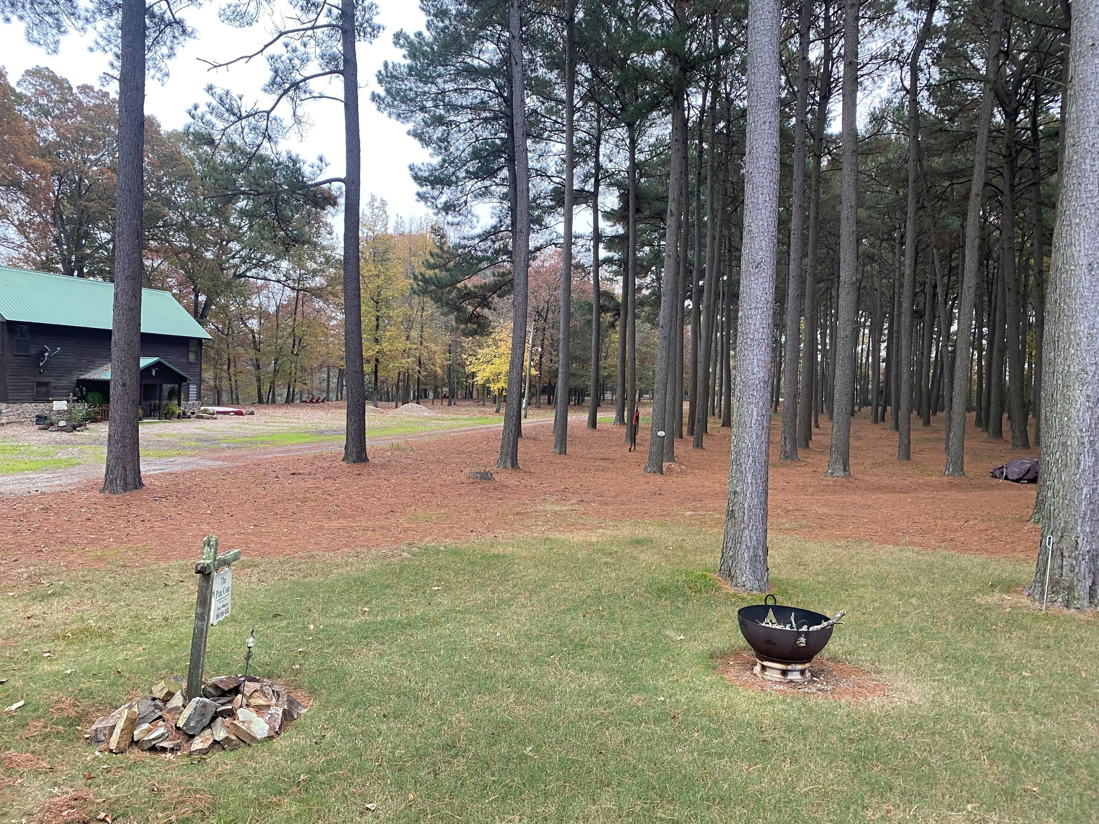 A forested area with a cabin, a fire pit, and a signpost.