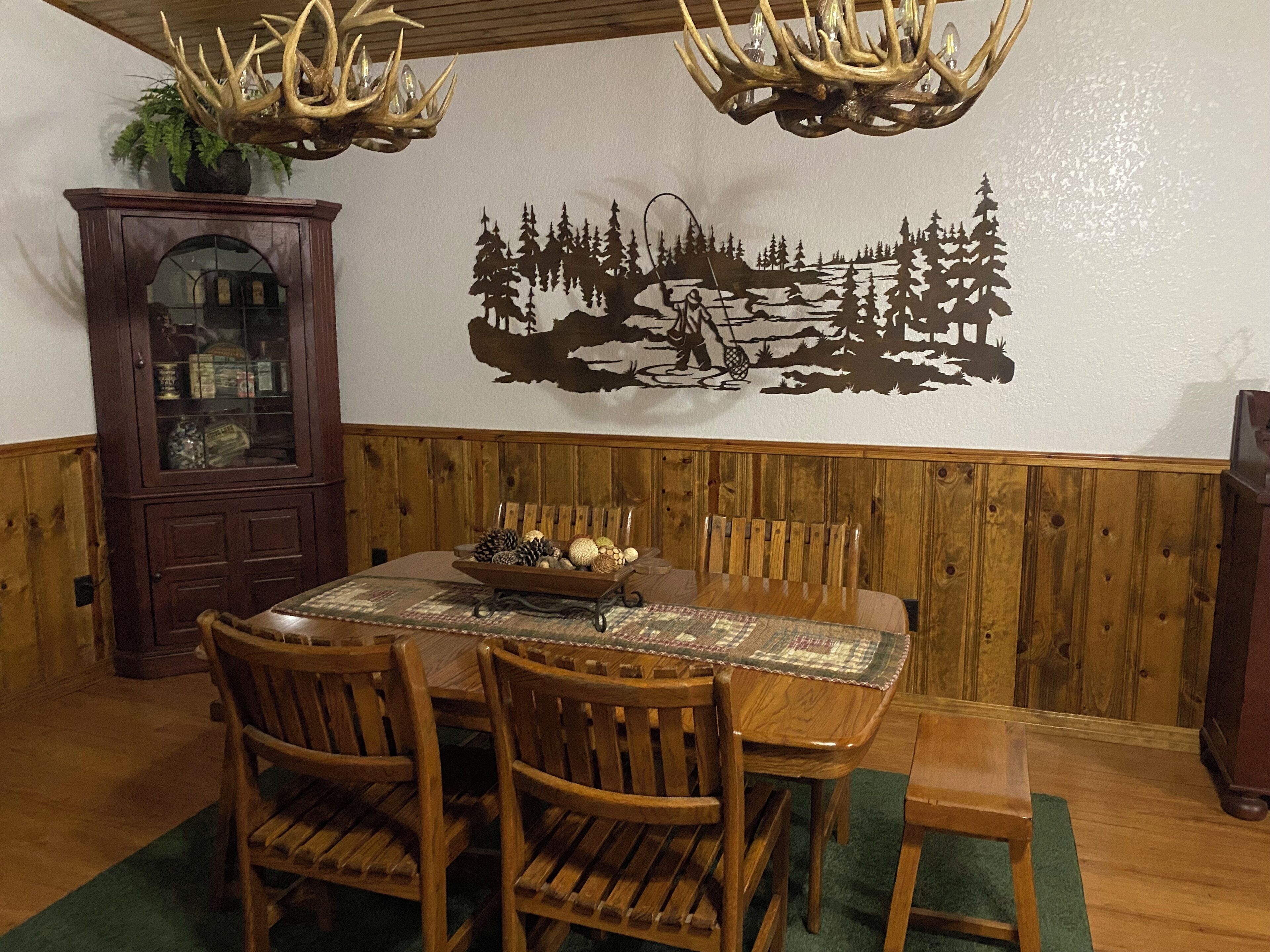 Zona pranzo con tavolo in legno, sedie, un lampadario e un affresco al muro.