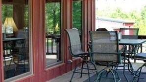 Eine überdachte Terrasse mit Sitzgelegenheiten im Freien, darunter Metallstühle und ein Tisch, sowie ein Schild, das die Flussrichtung angibt.