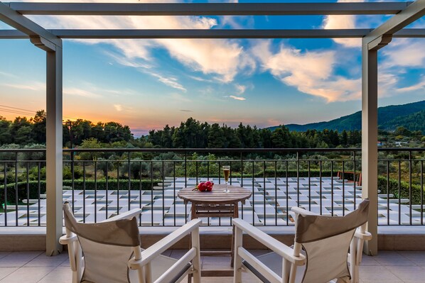 A terrace with two chairs, a table with fruit and a drink, and a view of a mountainous landscape.