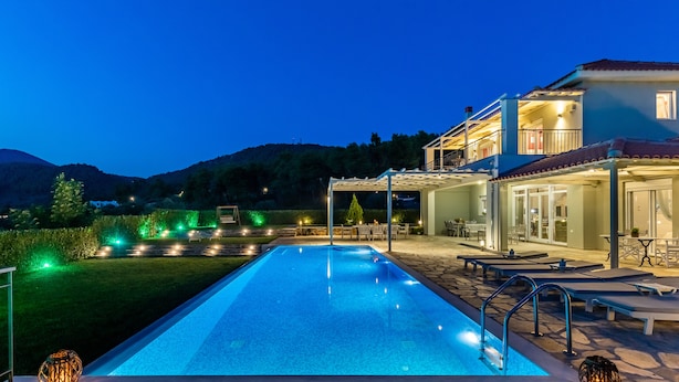 A swimming pool with a stone deck, outdoor seating, and a covered area with tables and chairs.