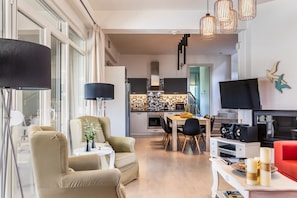A modern living room with a sofa, a dining table, and a kitchen in the background.