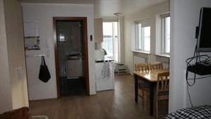 A compact living space with a kitchenette, dining area, and a TV mounted on the wall. - Nice Holiday Apartment, Centrally Located With Spectacular Sea And Mountain View (Akureyri)