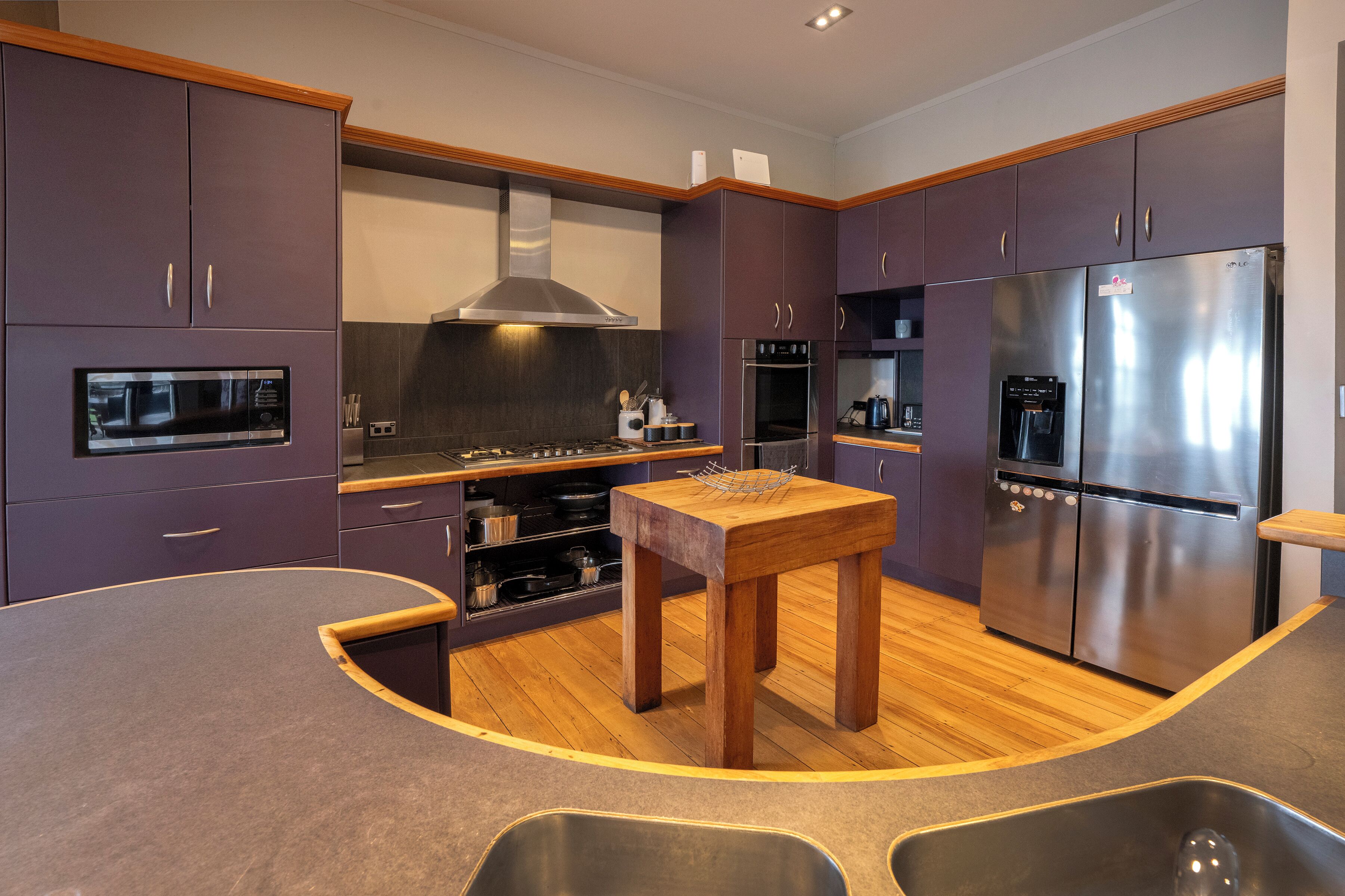 A modern kitchen with purple cabinets, stainless steel appliances, and a wooden island.