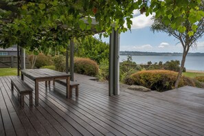 A wooden deck with a table and benches, surrounded by greenery and overlooking a body of water. - Lounge to Lake - Water's Edge, Lake Rotorua (Ngongotaha)