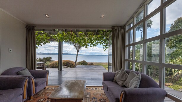 Ein modernes Wohnzimmer mit zwei Sofas, einem Couchtisch und einem großen Fenster mit Blick auf einen See und Grünflächen.