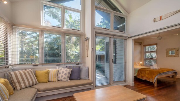Ein großzügiges Wohnzimmer mit großem Fenster, einer Couch mit Kissen, einem Couchtisch aus Holz und Blick ins Freie.