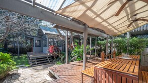 Eine Holzterrasse mit Tisch und Stühlen, umgeben von üppiger Vegetation und einem Haus im Hintergrund.