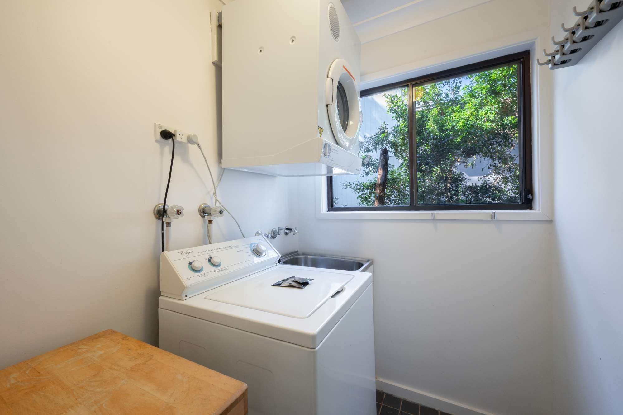 Une buanderie équipée d’un lave-linge et d’un sèche-linge à chargement frontal, d’une fenêtre donnant sur les arbres et d’une petite table.