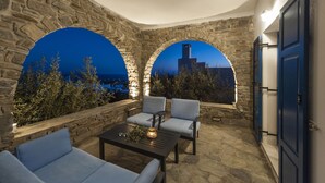 A stone-walled outdoor seating area with two arched windows overlooking a cityscape at dusk. - Pure White Villa: 7 Bedrooms, 16 Guests, Sea View, Aspro Chorio Village


 (Egeo)