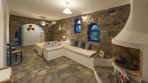 A cozy living room with a stone wall, a built-in fireplace, and a seating area with cushions. - Pure White Villa: 7 Bedrooms, 16 Guests, Sea View, Aspro Chorio Village


 (Egeo)