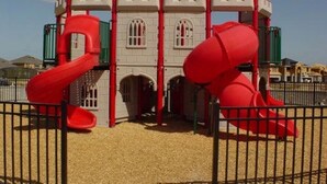 Een speeltuin met een kasteelachtige constructie, glijbanen en een omheind gebied.