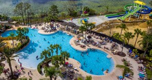 Une grande piscine extérieure dotée de plusieurs couloirs, entourée de palmiers et agrémentée d’espaces ombragés.