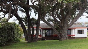 A small, single-story building with a sloped roof, surrounded by mature trees.