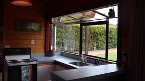 A kitchen with a stove, sink, and large windows overlooking a garden.