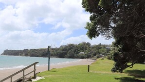 A coastal landscape with a grassy area, a wooden staircase leading to a beach, and a view of the sea and distant hills.