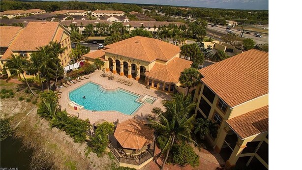 A resort with a central swimming pool, multiple buildings with red-tiled roofs, and surrounding greenery. - Beautiful Naples Condo (Naples)