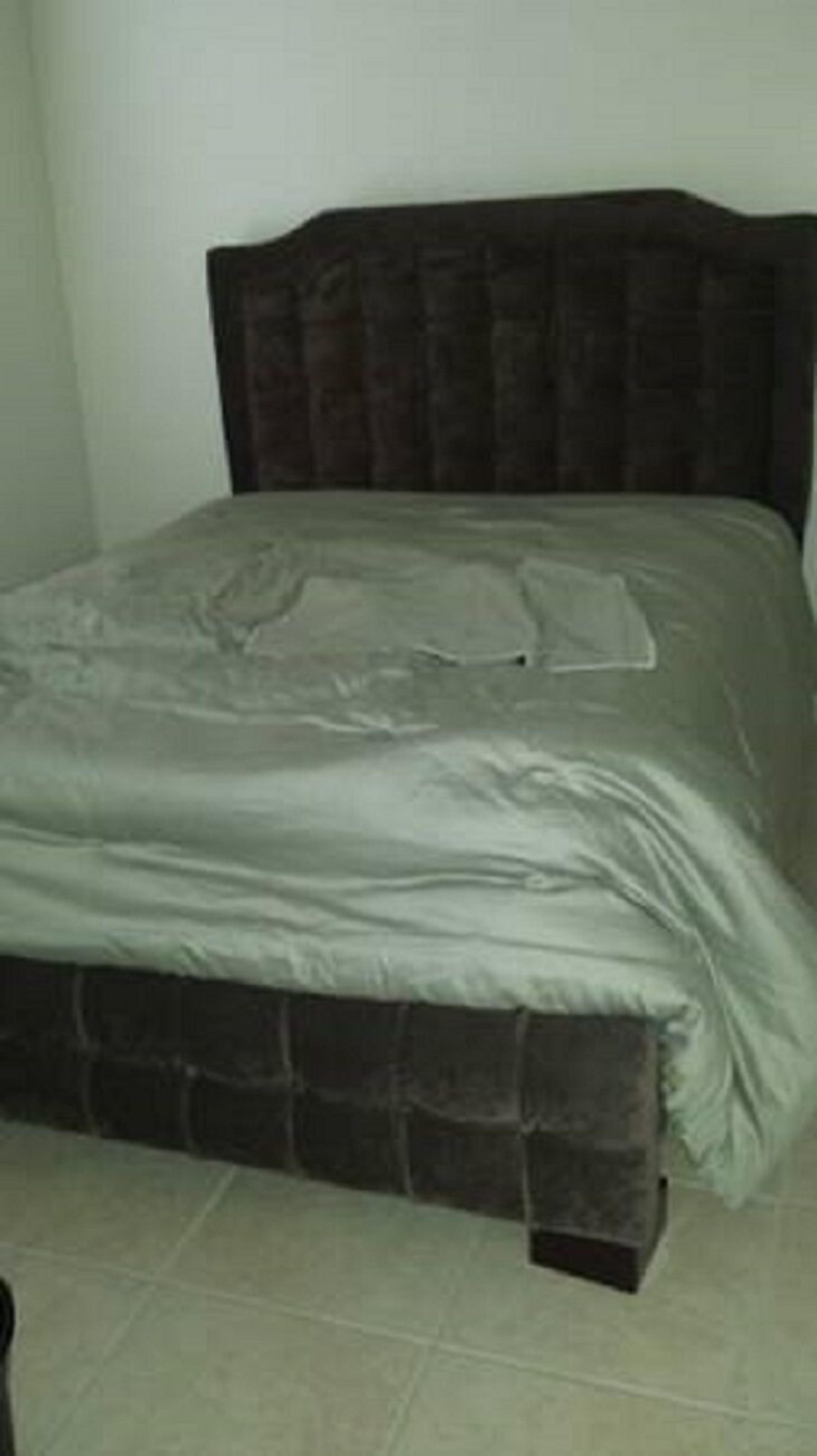 A bed with a dark headboard and a light-colored mattress.