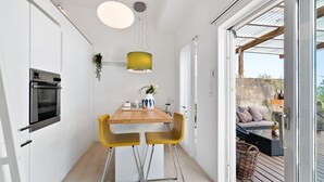 A compact kitchen with a wooden table, two yellow chairs, and a hanging green pendant light. - Bungalow by The Sea (Trondheim)