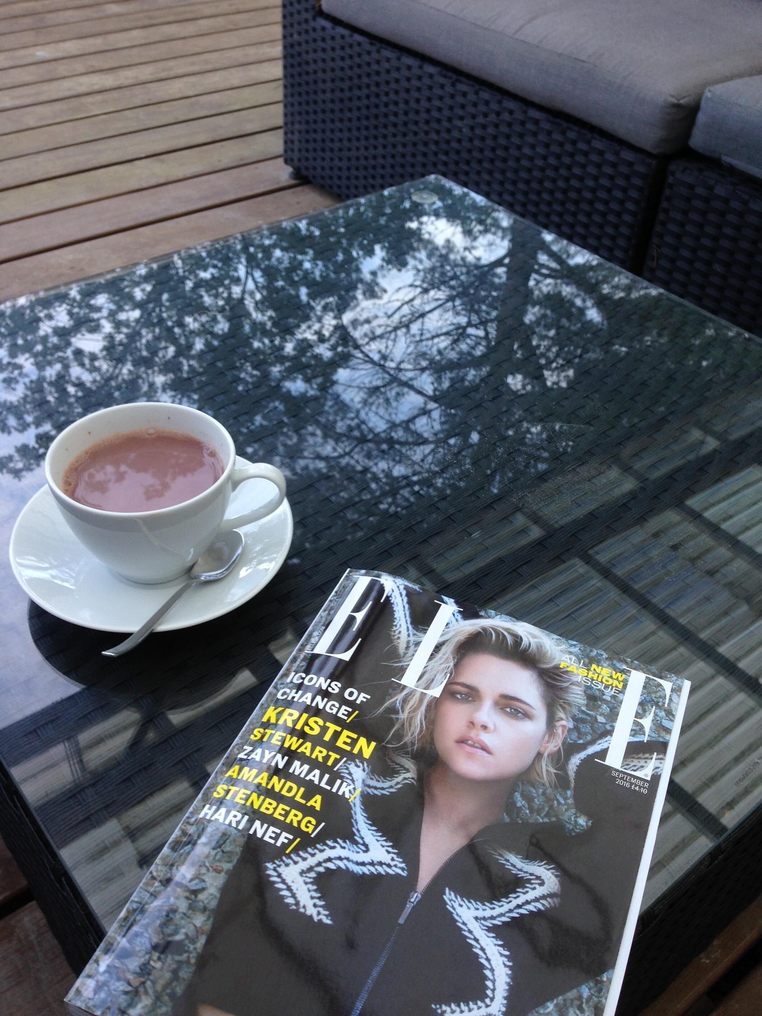 A magazine on a glass table with a cup of tea beside it.