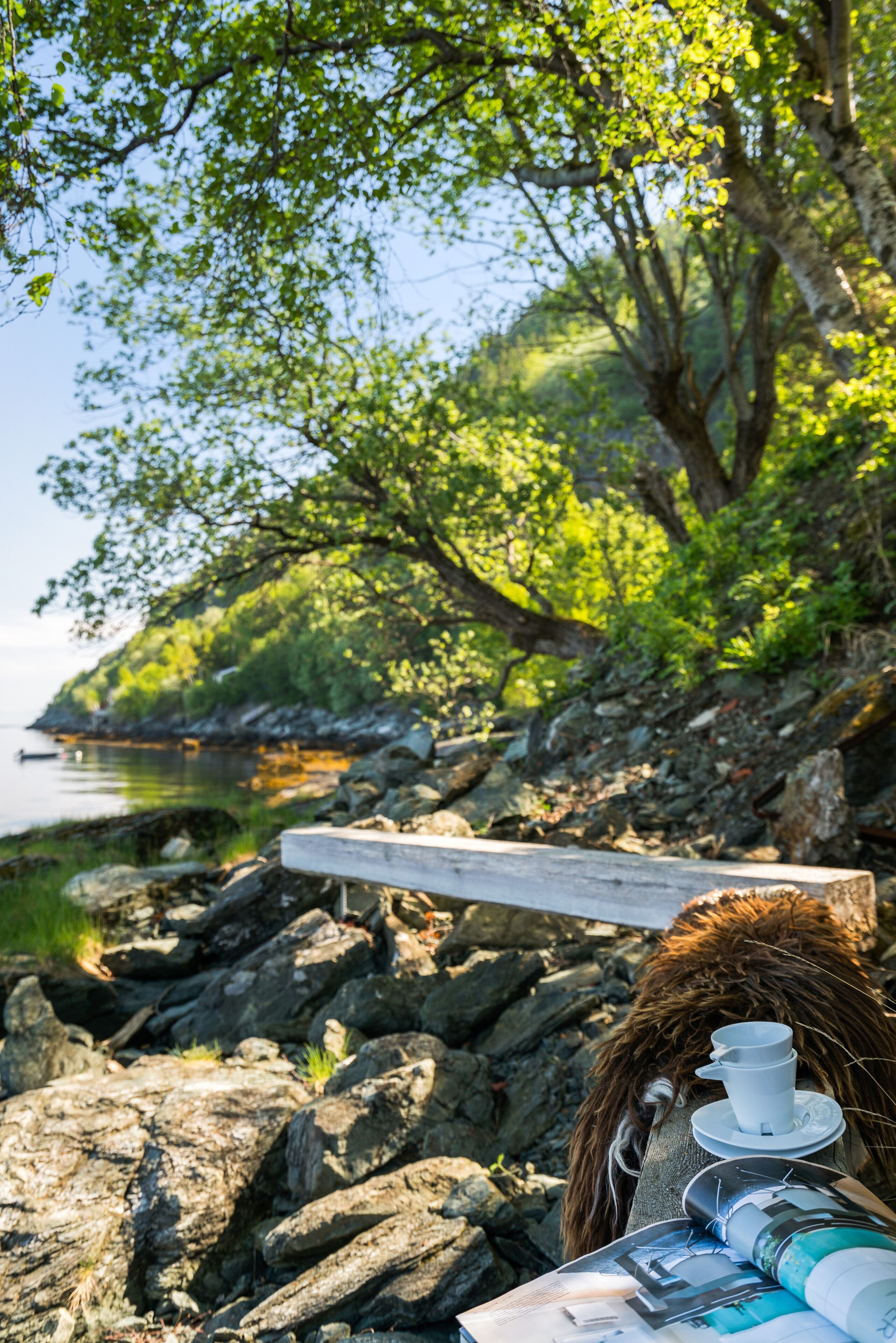 Un rivage rocheux avec un banc en bois et une table sur laquelle se trouvent une tasse et une soucoupe.