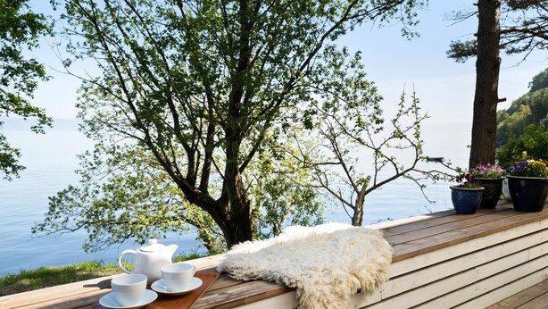 A wooden deck with a white furry throw blanket, a wooden tray with white cups and saucers, and potted plants. - Bungalow by The Sea (Trondheim)