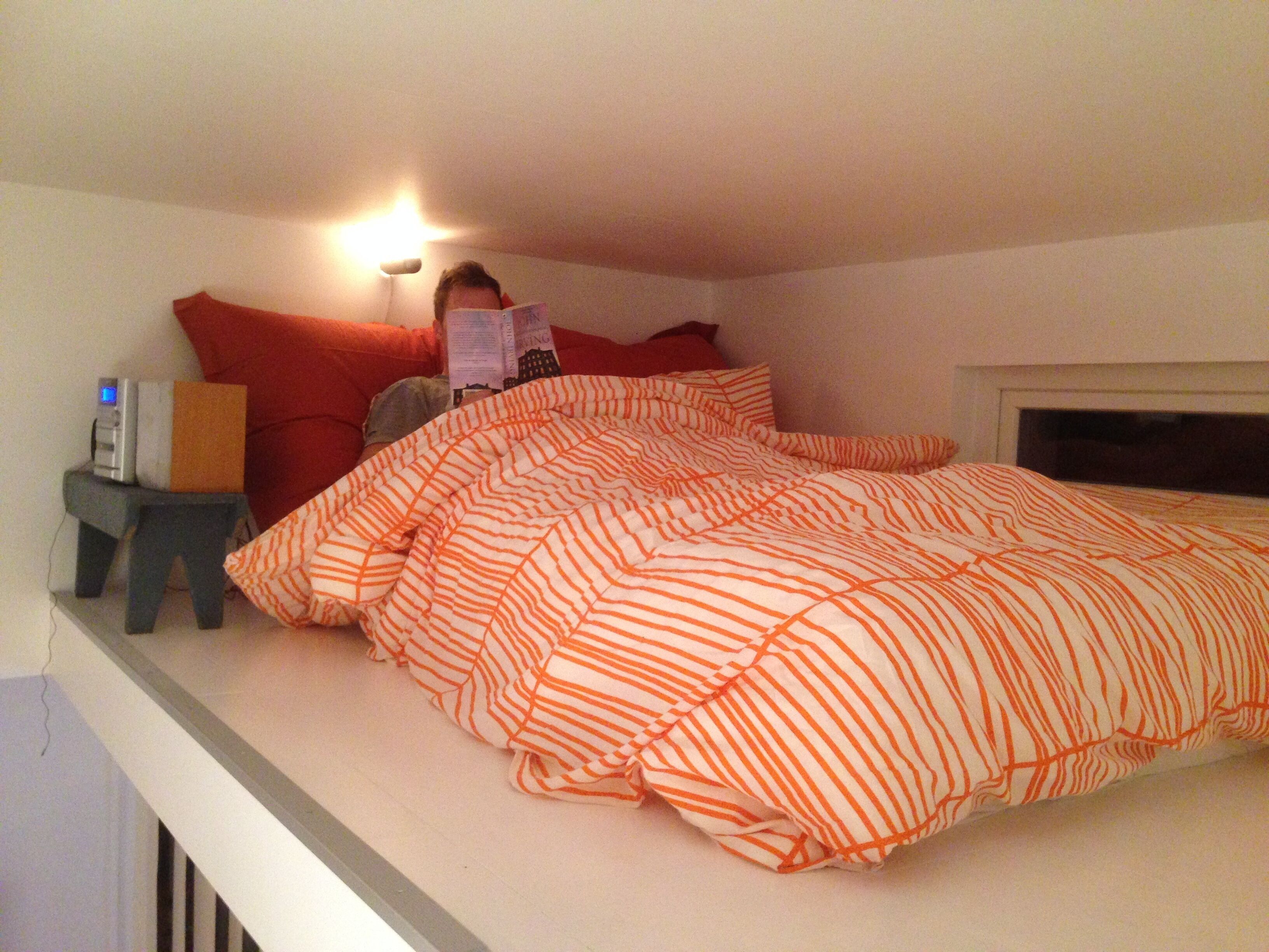 Un dormitorio con una cama cubierta con ropa de cama a rayas, una mesita de noche con una lámpara y un mueble auxiliar con un reloj.