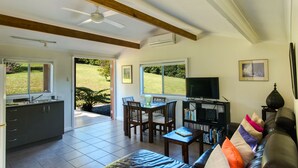 Un vaste espace de vie comprenant une table à manger, un canapé et un téléviseur. De grandes fenêtres offrent une vue sur un jardin.
