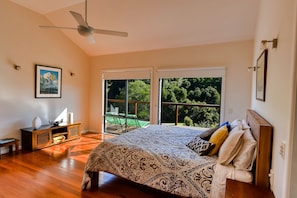 Relax in this serene bedroom with a large bed, ceiling fan, and sliding door leading to an outdoor area with a view.