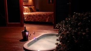 Un bain à remous sur une terrasse en bois, avec un lit en arrière-plan.