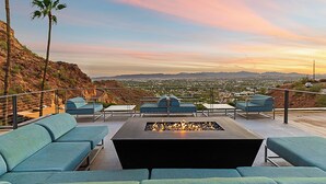 Eine Dachterrasse mit Sitzgelegenheiten im Freien und einem Feuerkorb, mit Blick auf eine Stadtlandschaft und Berge.
